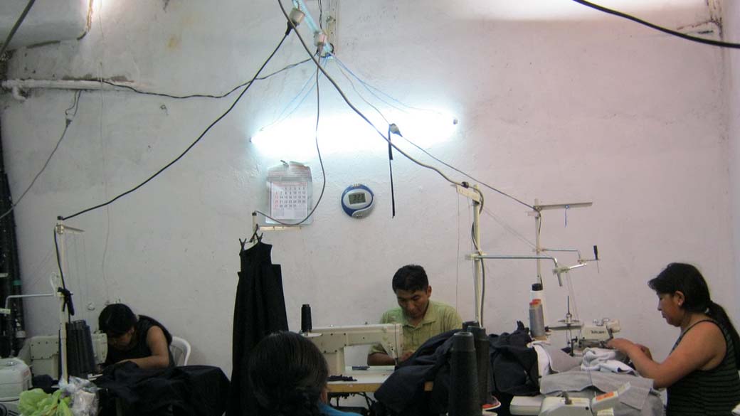Em foto divulgada pela Secretária da Justiça, trabalhadores bolivianos produzem peças para as Lojas Pernambucanas. De acordo com informações da secretária, os trabalhadores vivem em condições precárias dentro do próprio local onde confeccionam peças para a empresa