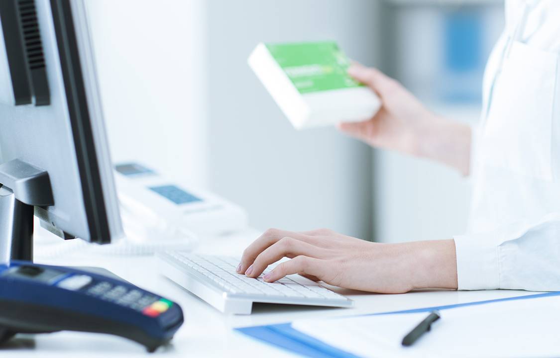 Pharmacist holding a medicine packet and searching that product in the computer database, healthcare and technology concept