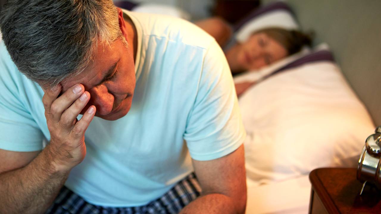 Homem sofrendo de insônia sentado na cama