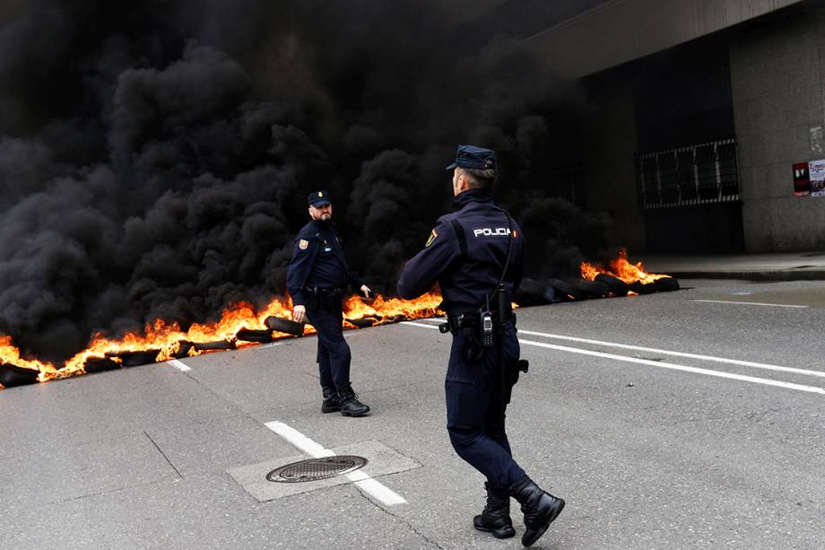 Policiais caminham em frente a uma barricada feita por manifestantes durante protestos do Dia do Trabalho em Gijón, Espanha Policiais caminham em frente a uma barricada feita por manifestantes durante protestos do Dia do Trabalho em Gijón, Espanha