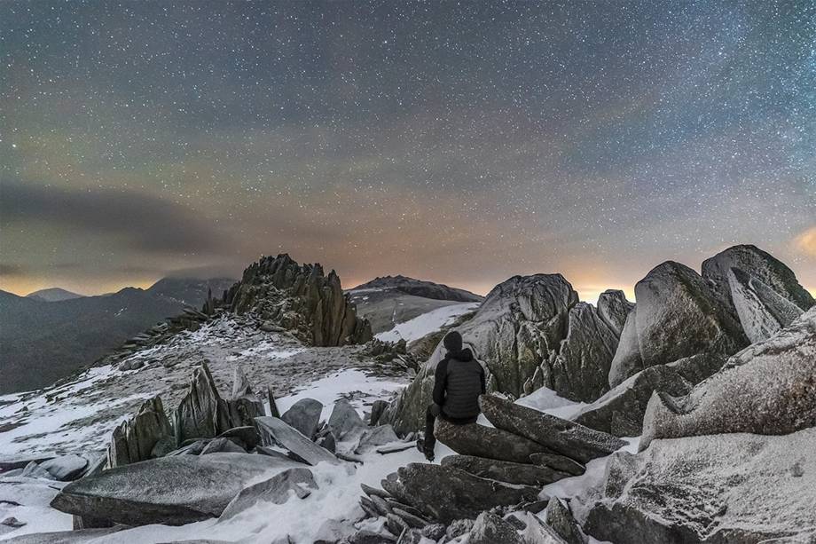 Observador solitário observando o céu estrelado em uma manhã fria no topo do Castelo dos Ventos, na montanha <span>Glyder Fach, no País de Gales. Para tirar essa foto, o fotógrafo montou seu equipamento e aguardou cerca de 15 horas no escuro, a -10ºC. Os 20 minutos em que o céu clareou foram suficientes para registrar a imagem.</span>