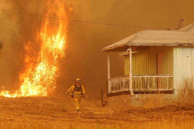 Um bombeiro passa ao lado de uma casa enquanto as chamas do incêndio Detwiler se aproximam rapidamente, na cidade de Mariposa, Califórnia Um bombeiro passa ao lado de uma casa enquanto as chamas do incêndio Detwiler se aproximam rapidamente, na cidade de Mariposa, Califórnia