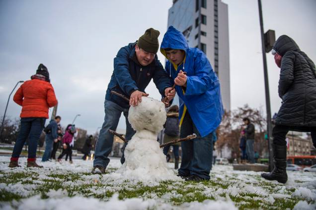 Pai e filho constróem boneco de neve em uma praça no centro de Santiago, após forte nevasca atingir a região, no Chile - 15/07/2017 Pai e filho constróem boneco de neve em uma praça no centro de Santiago, após forte nevasca atingir a região, no Chile - 15/07/2017