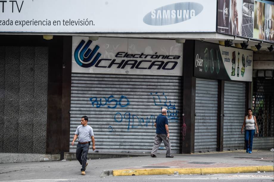 Pessoas passam em frente as lojas de portas fechadas devido à greve geral de 48 horas contra o presidente Maduro, em Caracas - 27/07/2017