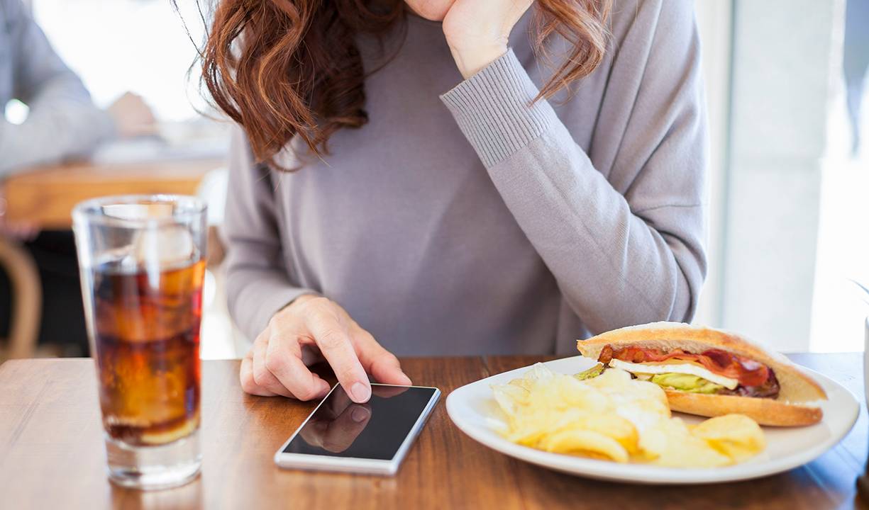 Mulher comendo e usando celular