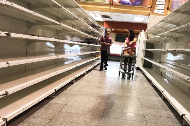 Mulheres caminham próximas de prateleiras vazias de supermercado em Caracas, na Venezuela - 09/01/2018