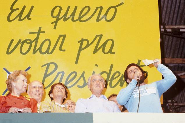 Em 25 de janeiro de 1984, ao lado de Ullysses Guimarães, André Franco Montoro, e suas respectivas esposas, Mora Guimarães e Lucy Franco Montoro, Lula participa do histórico comício na Praça da Sé, no Centro de São Paulo, para exigir a retomada das eleições para a presidência da República. O veto ao voto popular foi uma das medidas adotadas no período militar. Durante este regime, a escolha de presidentes e governadores ficaram a cargo da junta militar, por meio de eleições indiretas. Para se contrapor ao autoritarismo da Ditadura, criou-se o movimento “Diretas Já”, que embalou protestos e comícios em prol da redemocratização. Em 25 de janeiro de 1984, ao lado de Ullysses Guimarães, André Franco Montoro, e suas respectivas esposas, Mora Guimarães e Lucy Franco Montoro, Lula participa do histórico comício na Praça da Sé, no Centro de São Paulo, para exigir a retomada das eleições para a presidência da República. O veto ao voto popular foi uma das medidas adotadas no período militar. Durante este regime, a escolha de presidentes e governadores ficaram a cargo da junta militar, por meio de eleições indiretas. Para se contrapor ao autoritarismo da Ditadura, criou-se o movimento “Diretas Já”, que embalou protestos e comícios em prol da redemocratização.