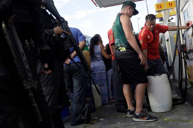 Policiais patrulham enquanto pessoas enchem vasilhas com gasolina em um posto de combustível no Rio de Janeiro - 28/05/2018 Policiais patrulham enquanto pessoas enchem vasilhas com gasolina em um posto de combustível no Rio de Janeiro - 28/05/2018