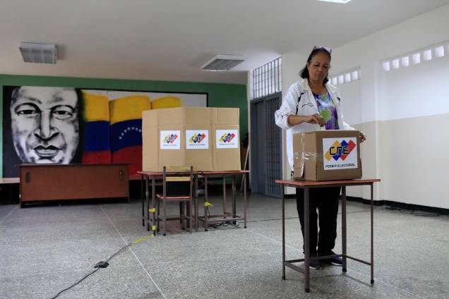 Com uma imagem do falecido presidente venezuelano, Hugo Chávez ao fundo, cidadã venezuelana vota durante a eleição presidencial em Caracas - 20/05/2018 Com uma imagem do falecido presidente venezuelano, Hugo Chávez ao fundo, cidadã venezuelana vota durante a eleição presidencial em Caracas - 20/05/2018