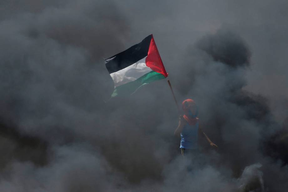 Manifestante segura uma bandeira palestina em meio a fumaça durante protesto contra a mudança da embaixada americana para Jerusalém - 14/05/2018 Manifestante segura uma bandeira palestina em meio a fumaça durante protesto contra a mudança da embaixada americana para Jerusalém - 14/05/2018