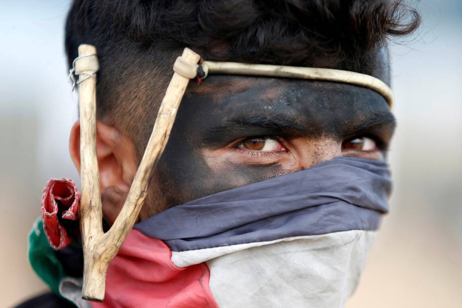 Manifestante palestino usa um estilingue durante protesto contra a mudança da embaixada dos Estados Unidos para Jerusalém e antes do 70º aniversário de Nakba, na fronteira entre Israel e Gaza, a leste da Cidade de Gaza - 14/05/2018