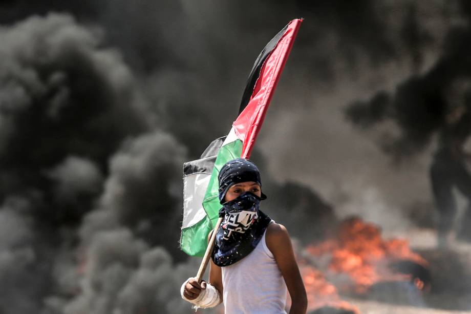 Menino Palestino segura bandeira durante confronto com tropas Israelenses na Faixa de Gaza - 14/05/2018 Menino Palestino segura bandeira durante confronto com tropas Israelenses na Faixa de Gaza - 14/05/2018
