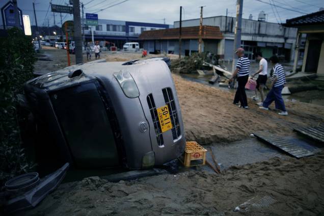 Moradores caminham ao lado de um carro danificado em uma área inundada em Kurashiki, província de Okayama, Japão - 08/07/2018 Moradores caminham ao lado de um carro danificado em uma área inundada em Kurashiki, província de Okayama, Japão - 08/07/2018