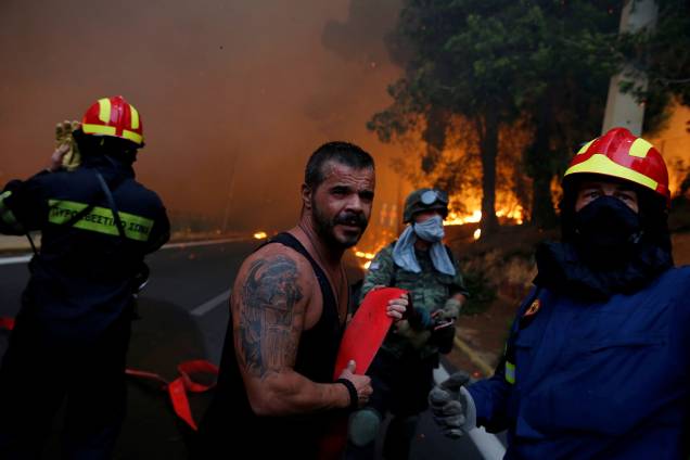 Bombeiros, soldados e moradores carregam uma mangueira enquanto um incêndio florestal atinge a cidade de Rafina, perto de Atenas, na Grécia - 23/07/2018 Bombeiros, soldados e moradores carregam uma mangueira enquanto um incêndio florestal atinge a cidade de Rafina, perto de Atenas, na Grécia - 23/07/2018