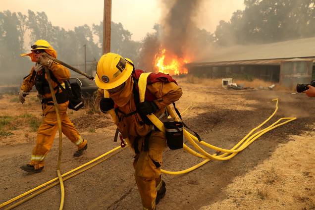 Bombeiros carregam mangueiras enquanto um celeiro arde nas chamas do incêndio River Fire em Lakeport, na Califórnia - 01/08/2018 Bombeiros carregam mangueiras enquanto um celeiro arde nas chamas do incêndio River Fire em Lakeport, na Califórnia - 01/08/2018