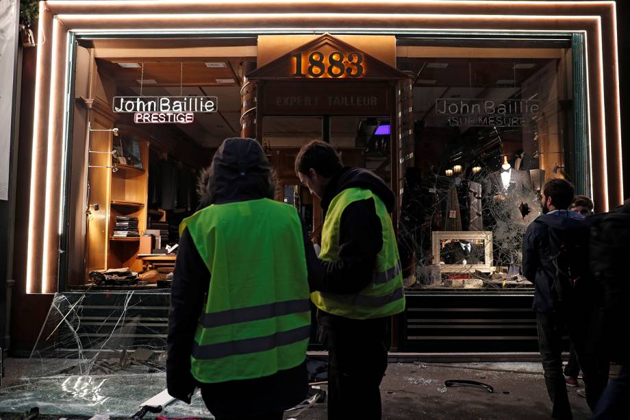 Manifestantes vestindo coletes amarelos param em frente a loja vandalizada durante manifestação em Paris, França - 08/12/2018