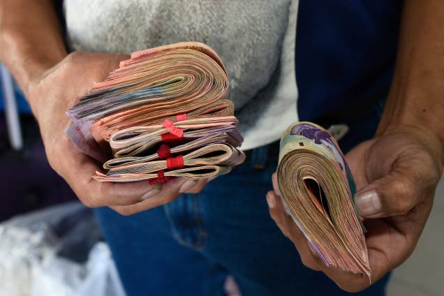 Homem segura cédulas de bolívar, a moeda oficial da Venezuela para pagar por uma passagem na rodoviária de Caracas - 03/01/2019 Homem segura cédulas de bolívar, a moeda oficial da Venezuela para pagar por uma passagem na rodoviária de Caracas - 03/01/2019