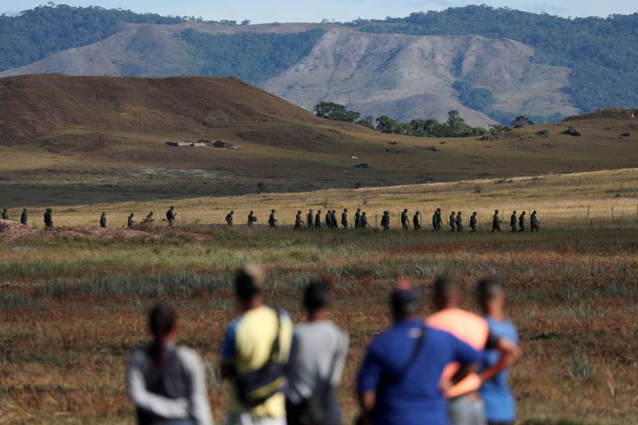 Pessoas observam militares venezuelanos enquanto andam próximos à fronteira entre Brasil e Venezuela no município de Pacaraima, Roraima - 22/02/2019