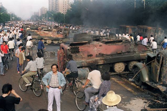 Chineses se reúnem perto dos restos mortais de mais de 20 veículos blindados queimados por manifestantes durante confrontos com soldados perto da Praça Tiananmen, em Pequim - 04/06/1989 Chineses se reúnem perto dos restos mortais de mais de 20 veículos blindados queimados por manifestantes durante confrontos com soldados perto da Praça Tiananmen, em Pequim - 04/06/1989