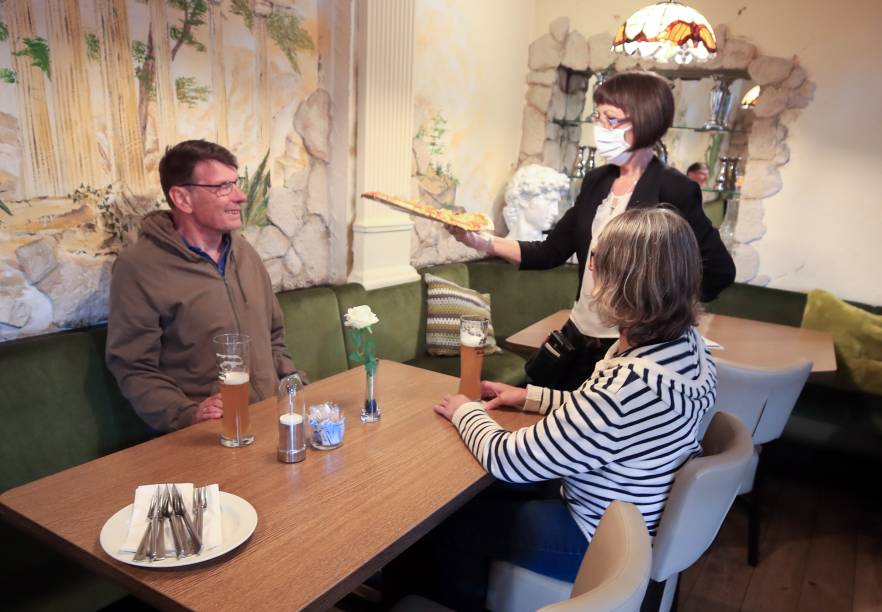 Garçom usa máscara para servir os clientes no restaurante Tuscolo, em Bonn, na Alemanha.