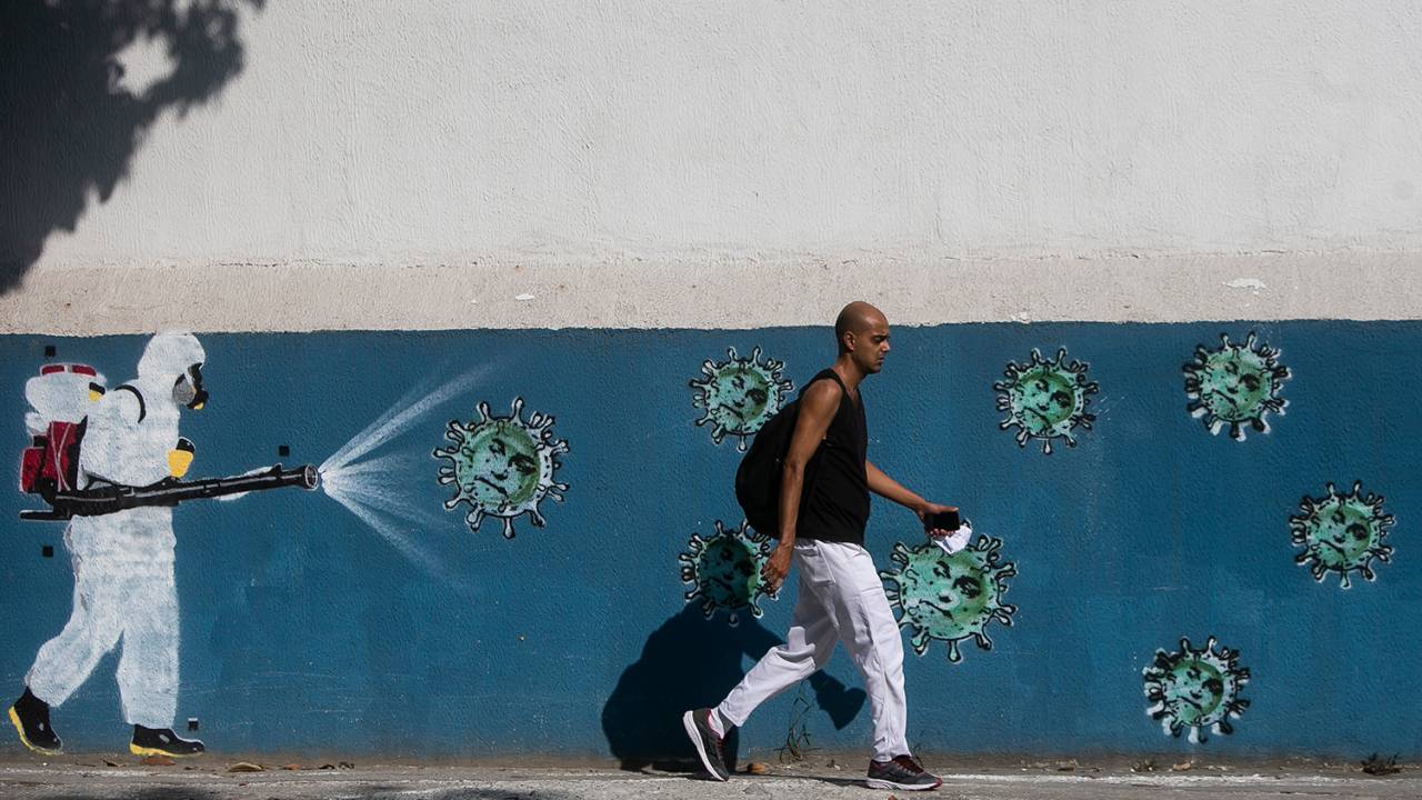 Um homem passa por uma parede com um grafite representando um limpador com equipamentos de proteção pulverizando vírus com o rosto do Presidente Jair Bolsonaro no bairro Estacio, no Rio de Janeiro