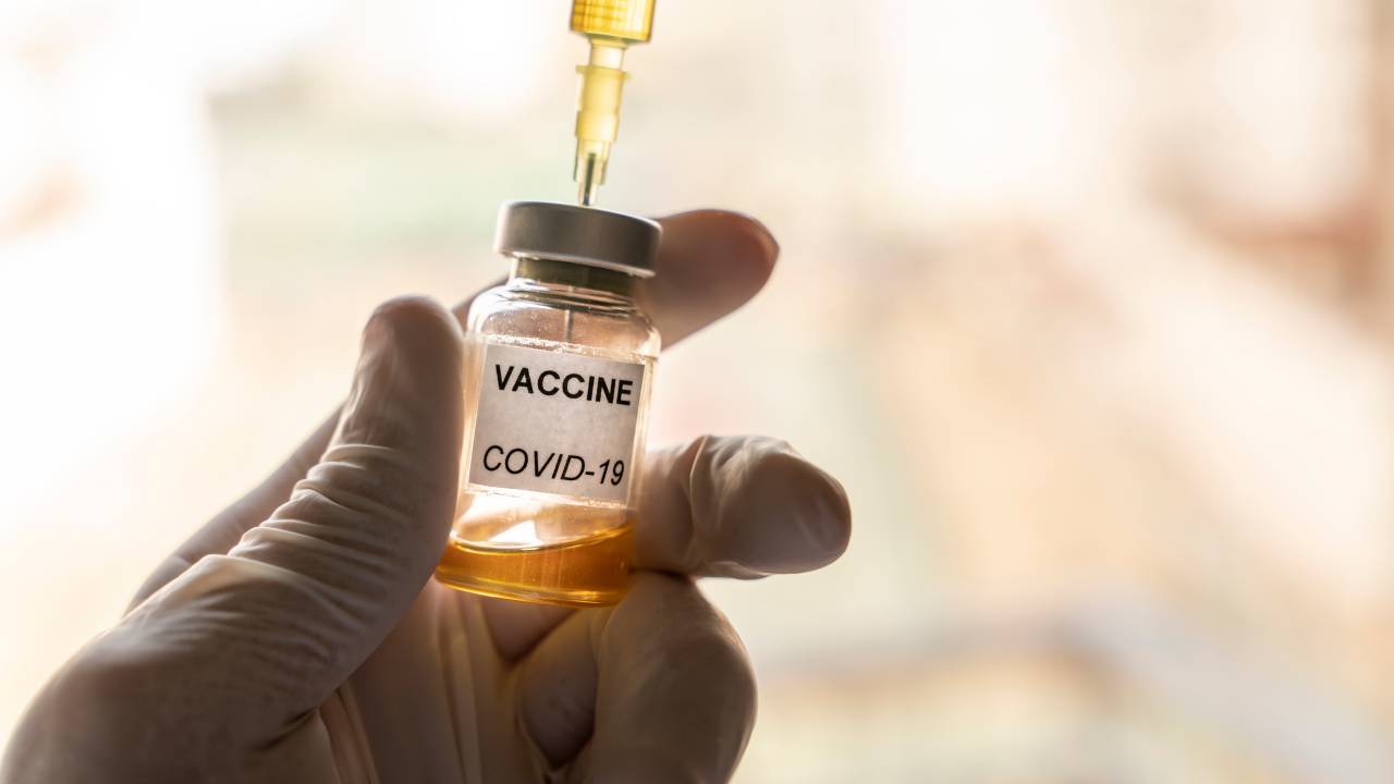 Cropped hand wearing a nitrile glove holding a Covid-19 vaccine vial and a syringe