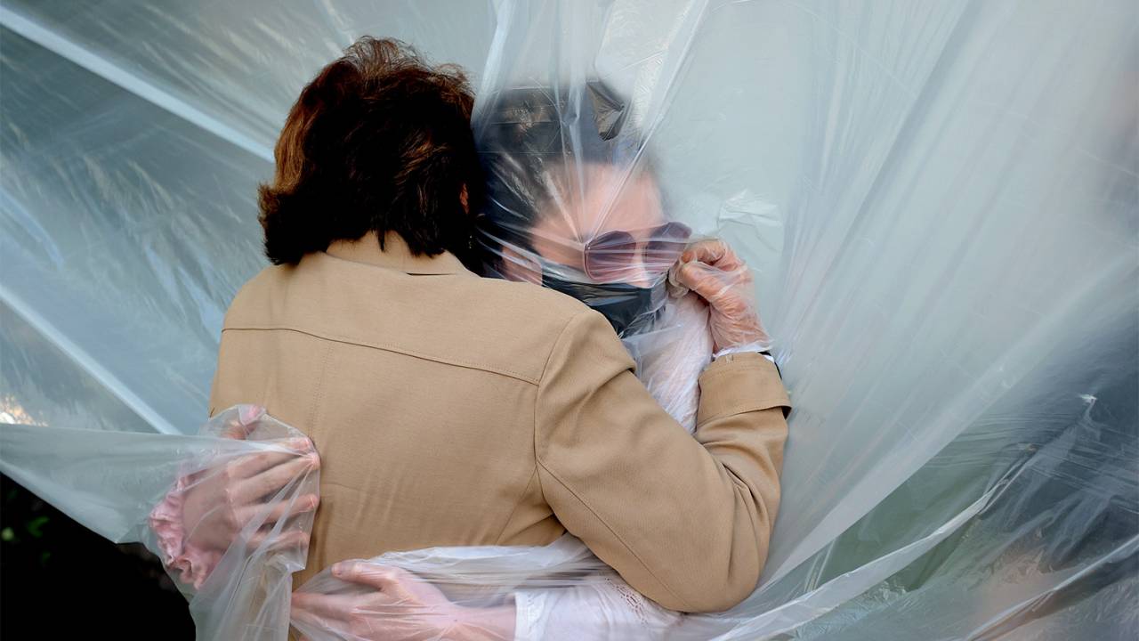 ISOLADAS - Filha abraça mãe protegida por plástico: medo de contágio -
