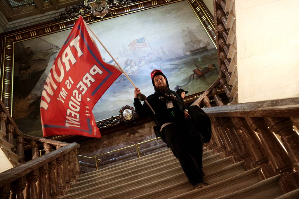 Um manifestante segura uma bandeira pr&oacute;-Trump dentro do edif&iacute;cio do Capit&oacute;lio, nos EUA -