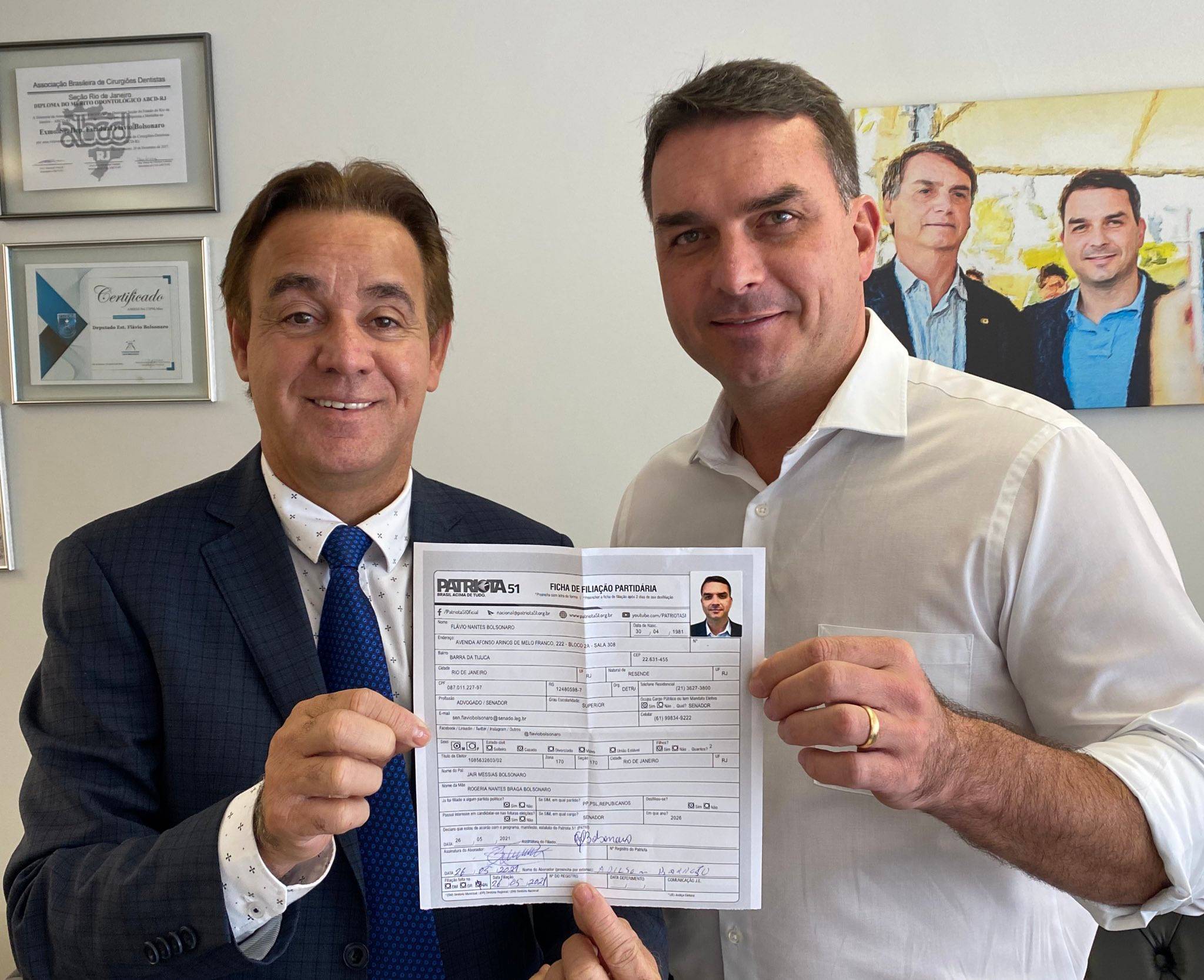 O presidente do Patriota, Adilson Barroso, e Flávio Bolsonaro exibem ficha de filiação do senador ao partido