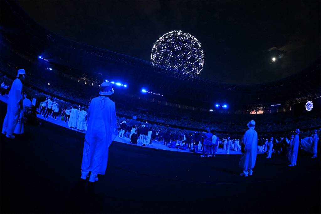 Atletas e volunt&aacute;rios olham drone no c&eacute;u durante a cerim&ocirc;nia de abertura das Olimp&iacute;adas 2020, no Est&aacute;dio Ol&iacute;mpico de T&oacute;quio -