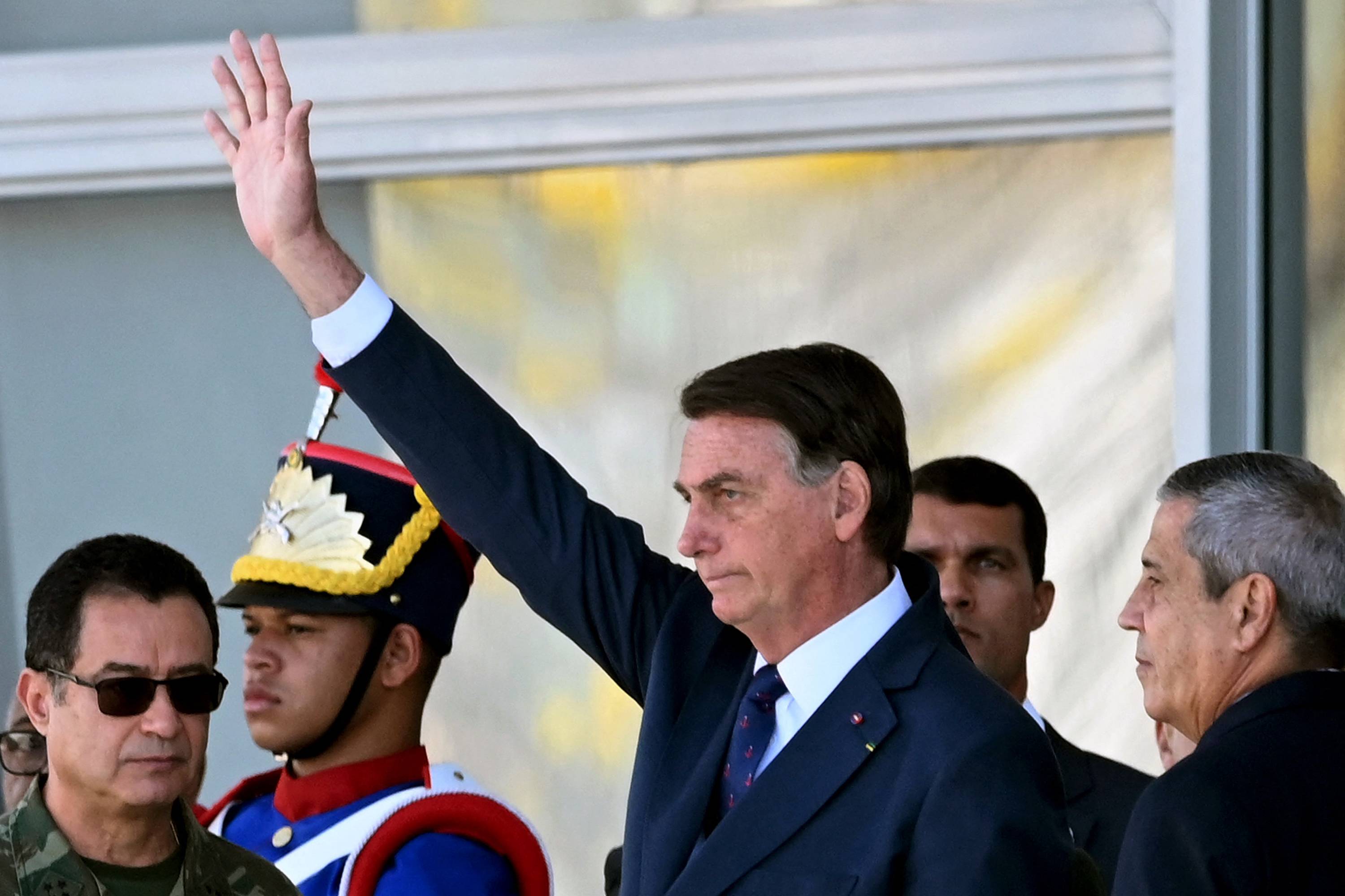Brazilian President Jair Bolsonaro (C) waves next to his Defense Minister Braga Netto (R), and Navy Commander Almir Garnier (L), during a military vehicles parade in front of the Planalto Palace in Brasilia, on August 10, 2021. - Bolsonaro is accused of using the armed forces for a show of force to intimidate National Congress, where a bill is being debated to modify the electronic voting system. (Photo by EVARISTO SA / AFP)