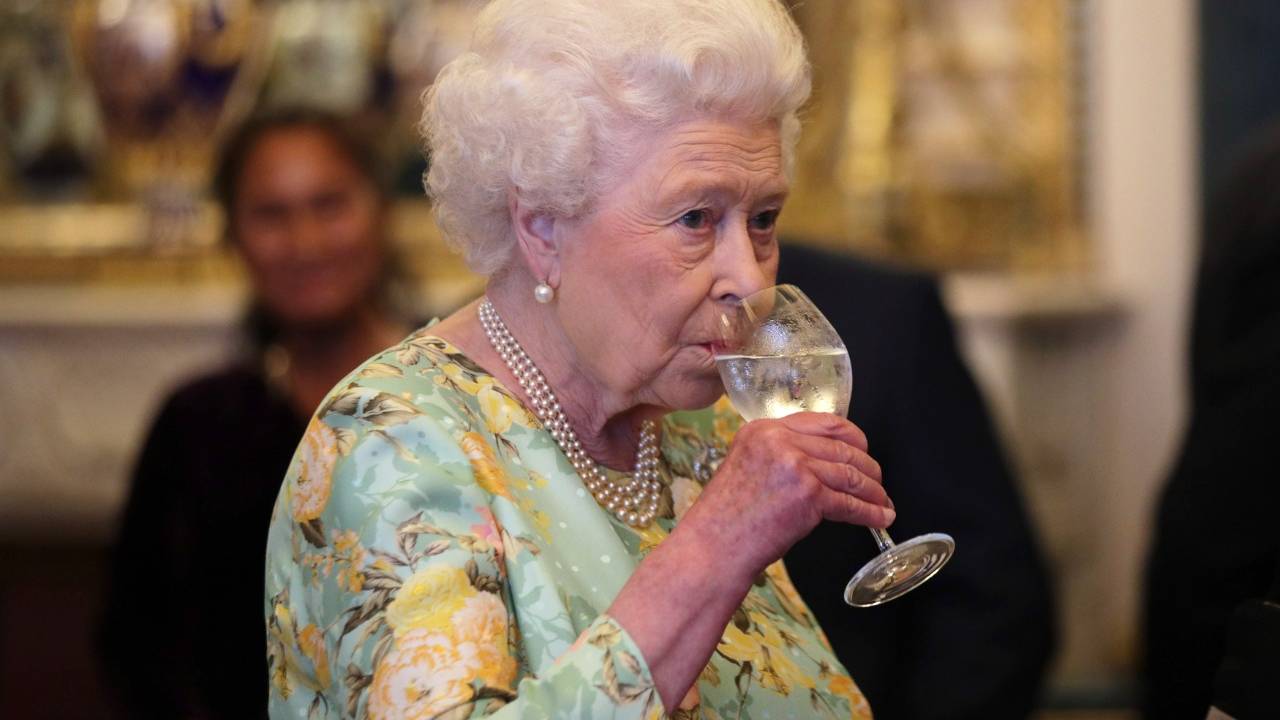 A imagem mostra a rainha elizabeth tomando uma taça de vinho