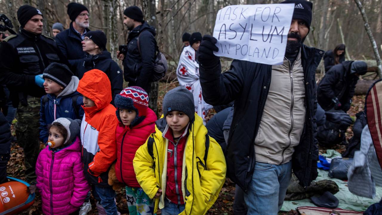 Membro de família iraquiana segura cartaz pedindo asilo na Polônia perto da fronteira entre Polônia e Belarus. 09/11/2021