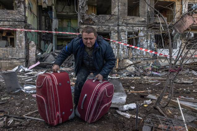 Um homem carrega bagagem do edifício residencial atingido pelo bombardeio da artilharia russa, em Kiev - Um homem carrega bagagem do edifício residencial atingido pelo bombardeio da artilharia russa, em Kiev -