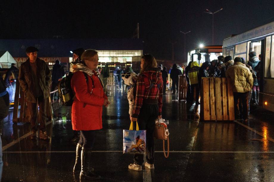 Pessoas aguardam ao lado de um ônibus enquanto um comboio de evacuação chega ao um centro de desalojados em Zaporizhzhia -