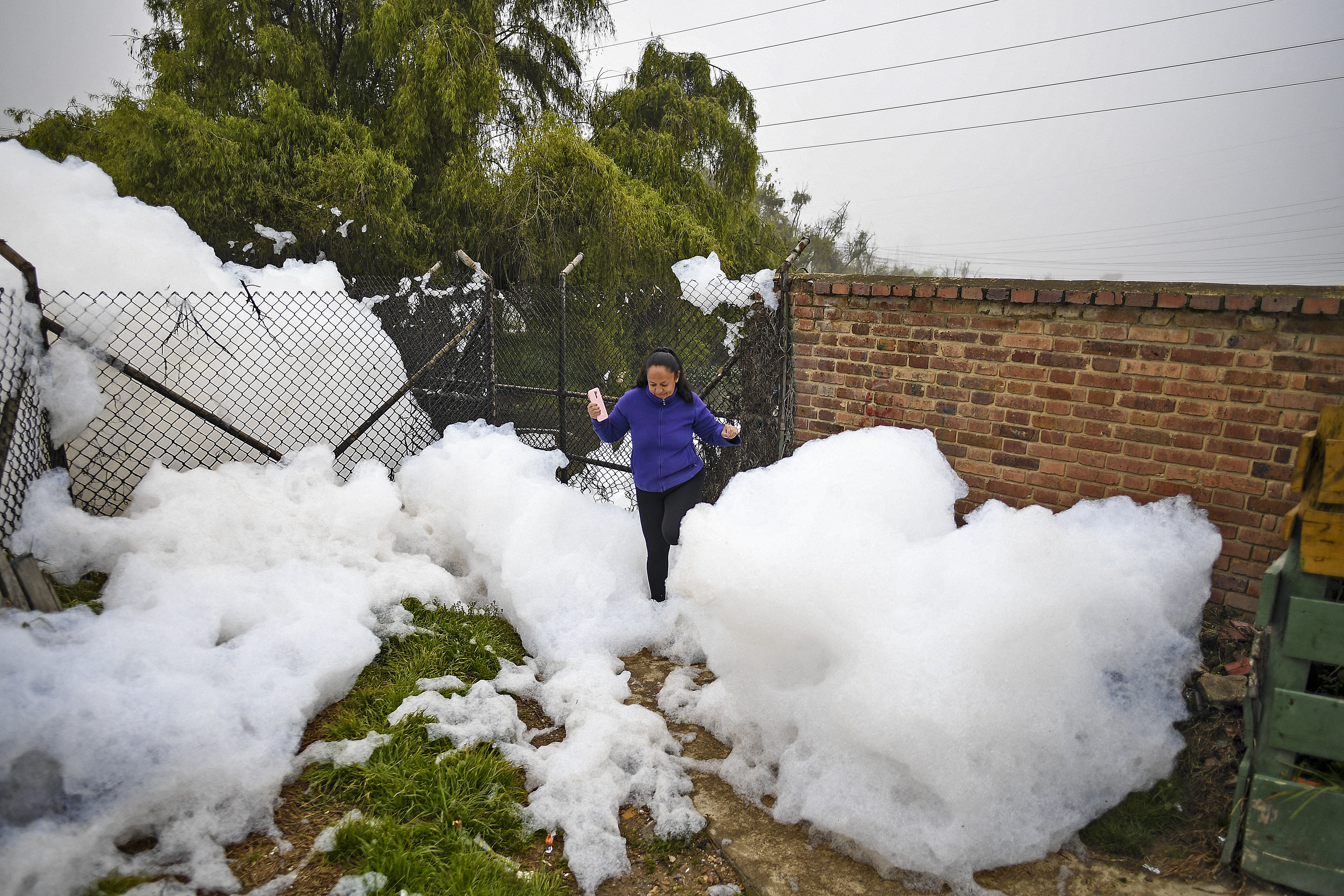 A woman walks through pungent foam which formed in a polluted river and invaded the Los Puentes neighbourhood, in Mosquera, west of Bogota, on April 26, 2022. (Photo by Juan BARRETO / AFP)
