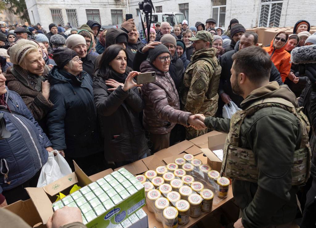 O presidente ucraniano Volodymyr Zelensky conversando com os moradores locais enquanto eles recebem ajuda humanit&aacute;ria -