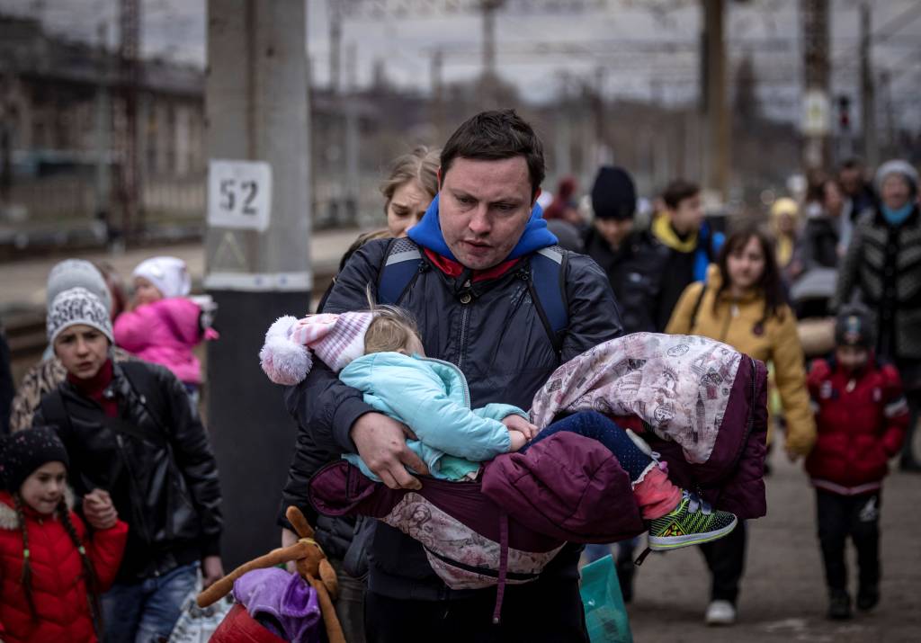 Um homem carrega uma menina ao chegar com outras fam&iacute;lias para embarcar em um trem na esta&ccedil;&atilde;o central de Kramatorsk -