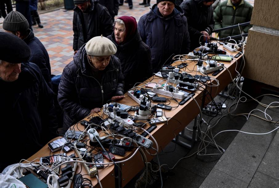 Pessoas carregando os seus celulares em um prédio público de Bucha -