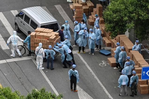 Trabalhadores usando equipamentos de proteção, empurram um carrinho cheio de caixas com alimentos para serem entregues em um bairro durante um bloqueio de Coronavírus Covid-19 no distrito de Jing'an, em Xangai, em 7 de maio de 2022. Trabalhadores usando equipamentos de proteção, empurram um carrinho cheio de caixas com alimentos para serem entregues em um bairro durante um bloqueio de Coronavírus Covid-19 no distrito de Jing'an, em Xangai, em 7 de maio de 2022.