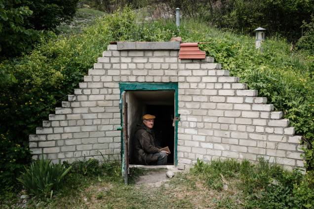 O professor de biologia ucraniano Oleksiy Polyakov, 84, lê o livro intitulado "200 Lugares Maravilhosos e Incríveis" na entrada de sua adega de vegetais transformada em abrigo em Sydorove, leste da Ucrânia, em 17 de maio de 2022. O professor de biologia ucraniano Oleksiy Polyakov, 84, lê o livro intitulado "200 Lugares Maravilhosos e Incríveis" na entrada de sua adega de vegetais transformada em abrigo em Sydorove, leste da Ucrânia, em 17 de maio de 2022.