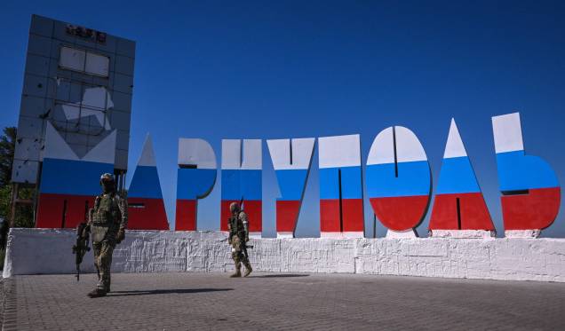 Militares russos caminham perto da placa de boas-vindas "Mariupol", com as cores da bandeira russa, em 12 de junho de 2022. Militares russos caminham perto da placa de boas-vindas "Mariupol", com as cores da bandeira russa, em 12 de junho de 2022.