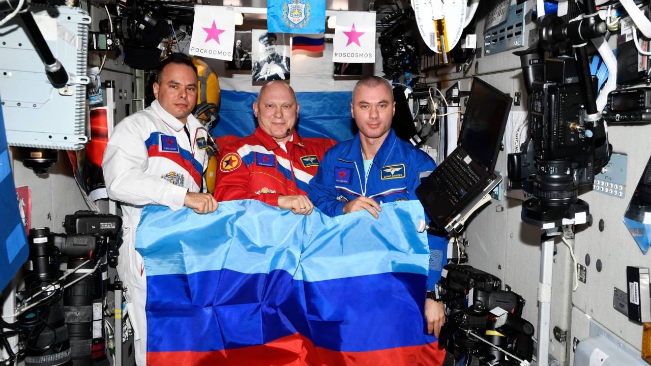 In this handout photo released by the Russian space agency Roscosmos on July 4, 2022 Russian cosmonauts Oleg Artemyev (C), Denis Matveyev (R) and Sergei Korsakov pose with a flag of the self-proclaimed Lugansk People's Republic onboard the International Space Station (ISS). - Russian cosmonauts held an east Ukrainian separatist flag onboard the ISS and congratulated Moscow's forces for capturing the whole of the Lugansk region from Kyiv, the Roscosmos space agency said on July 4, 2022. (Photo by Handout / Russian Space Agency Roscosmos / AFP) / RESTRICTED TO EDITORIAL USE - MANDATORY CREDIT "AFP PHOTO / Russian space agency Roscosmos / handout" - NO MARKETING NO ADVERTISING CAMPAIGNS - DISTRIBUTED AS A SERVICE TO CLIENTS