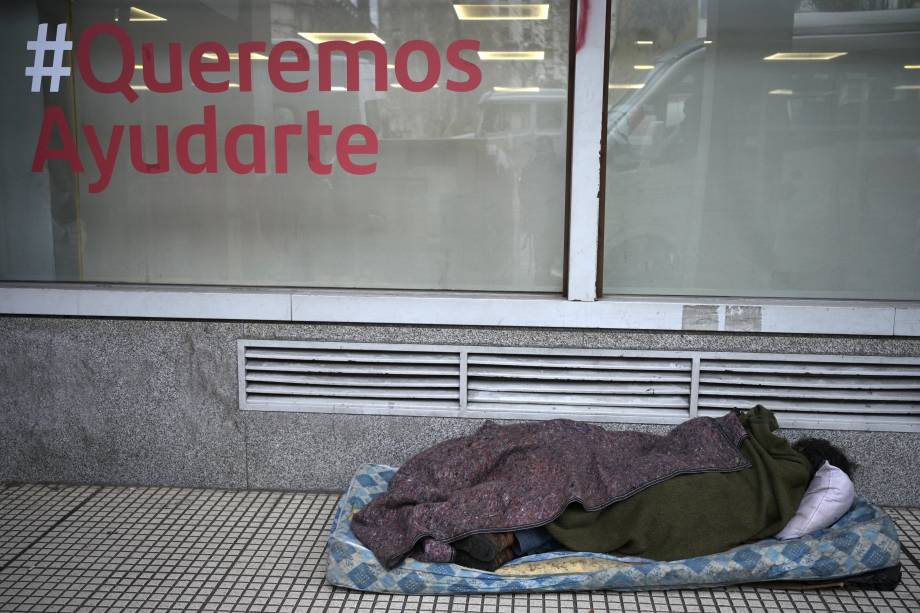 Uma pessoa dorme na calçada em frente `a um banco, com uma frase "Queremos ajudá-lo", no centro de Buenos Aires, em 11/07/2022. Uma pessoa dorme na calçada em frente `a um banco, com uma frase "Queremos ajudá-lo", no centro de Buenos Aires, em 11/07/2022.