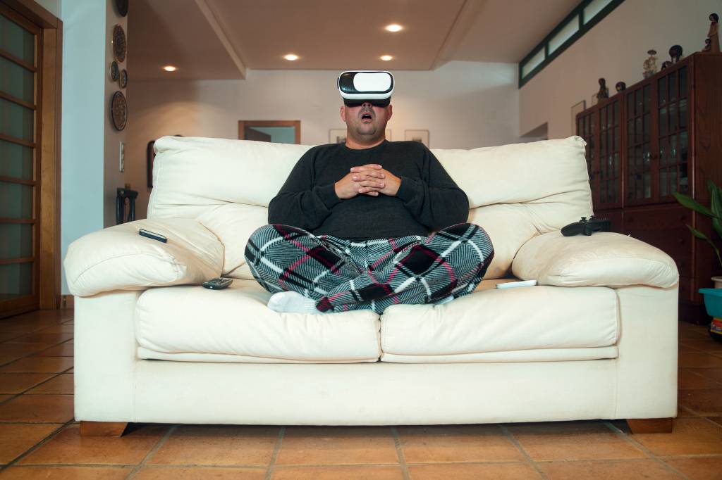 Adult man in pyjamas sitting on the sofa at home with virtual reality goggles AINDA NÃO - Atraso na hora de dormir: a estratégia para achar um tempo de lazer cresceu durante a pandemia de Covid-19 -