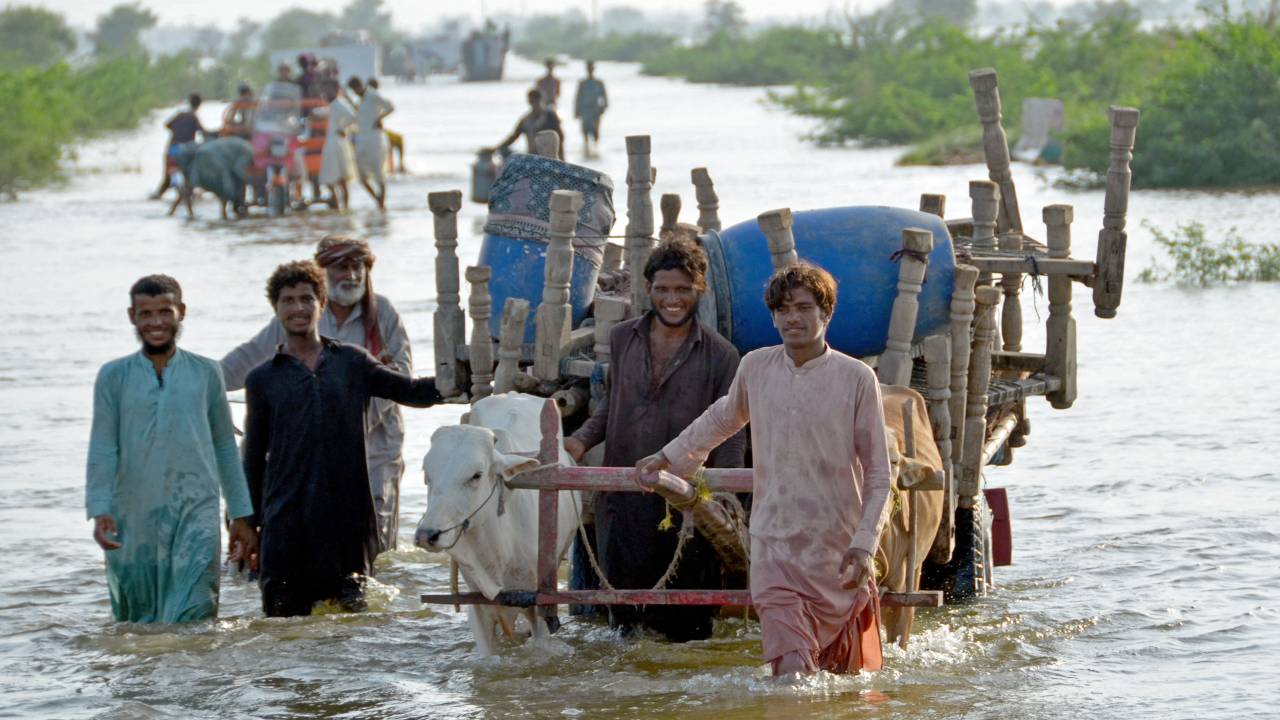 Stranded people along with their belongings wade through a flooded street after fleeing from their flood hit homes following heavy monsoon rains at Sohbatpur area in Jaffarabad district of Balochistan province on August 28, 2022. - Pakistan's flooded southern Sindh province braced on August 28 for a fresh deluge from swollen rivers in the north as the death toll from this year's monsoon topped 1,000. (Photo by Fida HUSSAIN / AFP)