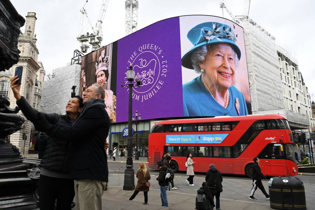 Um casal tira uma selfie enquanto as imagens da rainha Elizabeth II da Gr&atilde;-Bretanha s&atilde;o exibidas -