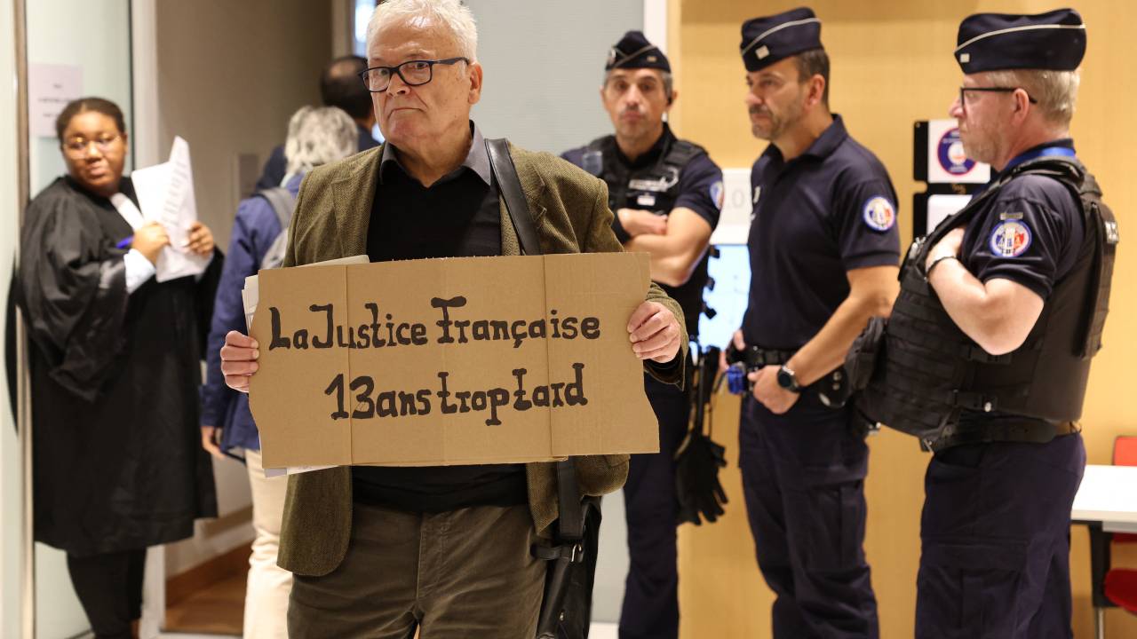 Um homem segura um cartaz com os dizeres "Justiça francesa, 13 anos atrasado" no tribunal de Paris em 10 de outubro de 2022 durante o julgamento das empresas Airbus e Air France pelo acidente do voo Rio-Paris Air France A330 em 1º de junho de 2009 que matou 228 pessoas.