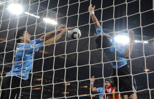 (FILES) In this file photo taken on July 2, 2010 Uruguay's striker Luis Suarez (L) stops the ball with the hand leading to a red card and a penalty for Ghana during the extra-time of 2010 World Cup quarter-final match Uruguay vs Ghana on July 2, 2010 at Soccer City stadium in Soweto, suburban Johannesburg. - Ghana say they have no plans to take revenge on Uruguay and Luis Suarez when they meet them on December 2, 2022 in the final matchday of World Cup Group H as they seek a place in the last 16. On 2 July 2010, Soccer City Stadium in Johannesburg hosted the quarter-final, which became one of the most dramatic and emotional World Cup matches of the 21st century. With the score at 1-1 at the end of the ninety minutes, there was nothing to suggest that the score would change in extra time. Then, in the 119th minute, came the most memorable play of South Africa 2010. Ghana had a free kick; the goalkeeper Fernado Muslera failed to take it and an African player headed and when the ball was going in, Luis Suarez, like a volleyball player, parried the ball with both hands and prevented the Celeste goal from falling. (Photo by ROBERTO SCHMIDT / AFP)