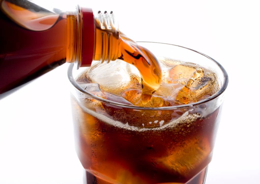 Soda (cola) being poured into plain glass with ice